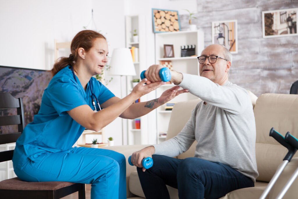 Senior man nursing home with doing physical therapy with help from nurse using dumbbells 1024x683
